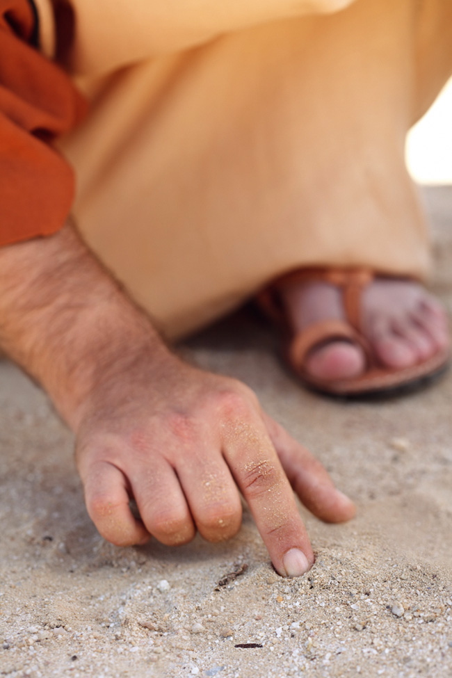 Homem com roupas dos tempos bblicos escrevendo na areia